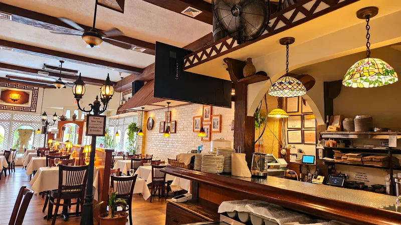 Bar counter with stained-glass pendant lamps and white tablecloth tables beyond