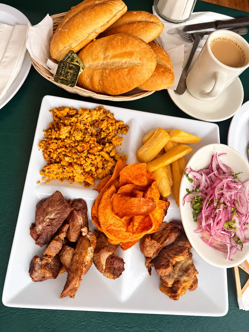Platter with fried pork, fried cassava, sweet potato, onion salad and a basket of bread