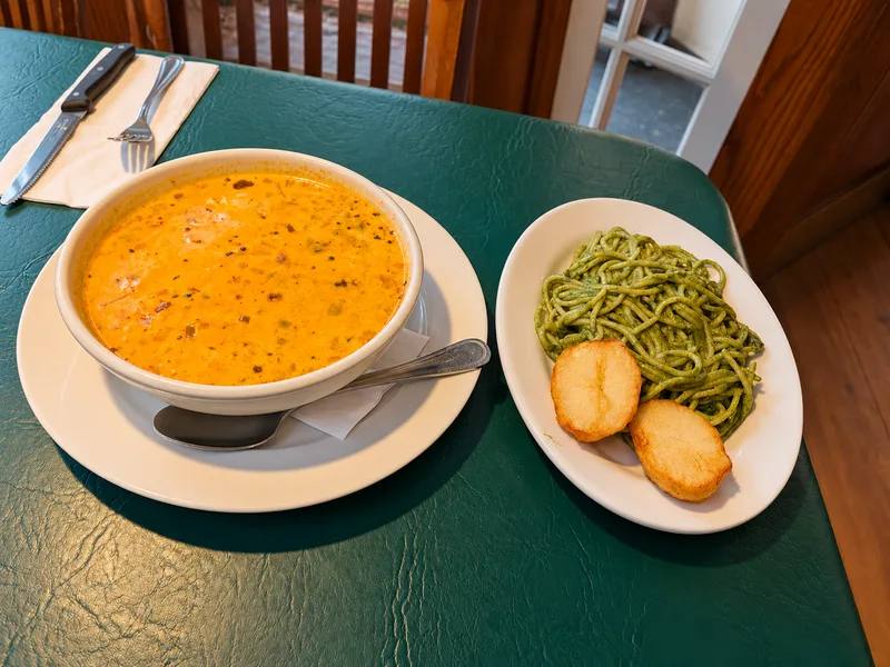 Bowl of creamy orange chowder beside a plate of green noodles with fried potato