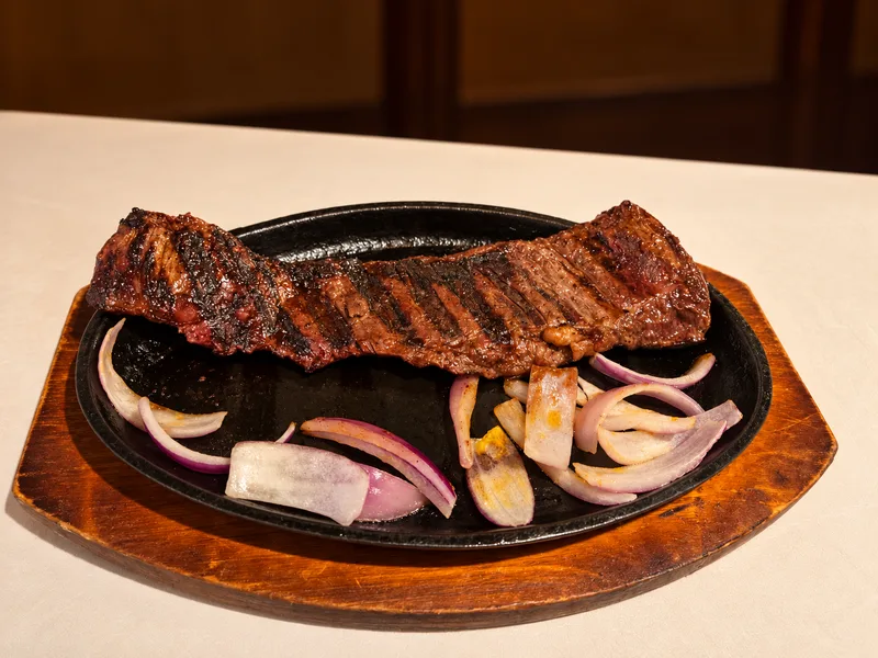 Grilled skirt steak with charred onions on a sizzling cast-iron plate
